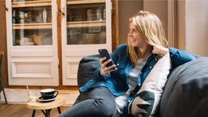 A person on the couch smiling as they browse their mobile phone